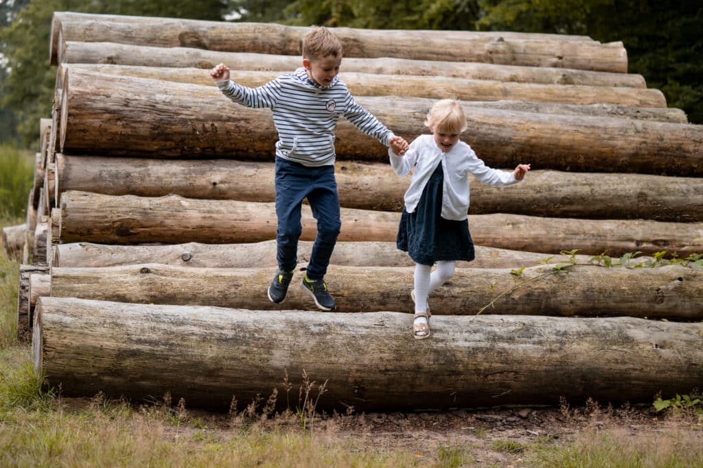 Zwei kleine Kinder springen händchenhaltend von einem Stammbaum. - Fotografin Köln finden